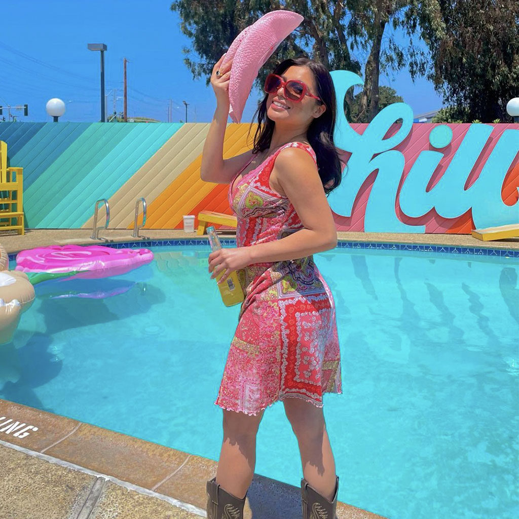 Girl in a pink dress and pink sunglasses tipping her pink cowboy hat in front of the CHILL sign at the pool of The Rambler Motel