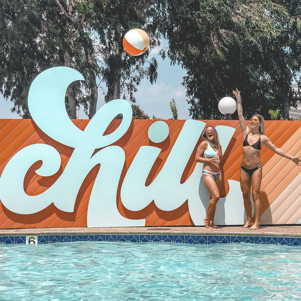 Two girls playing with a beach ball in front of the CHILL sign at the pool of The Rambler Motel