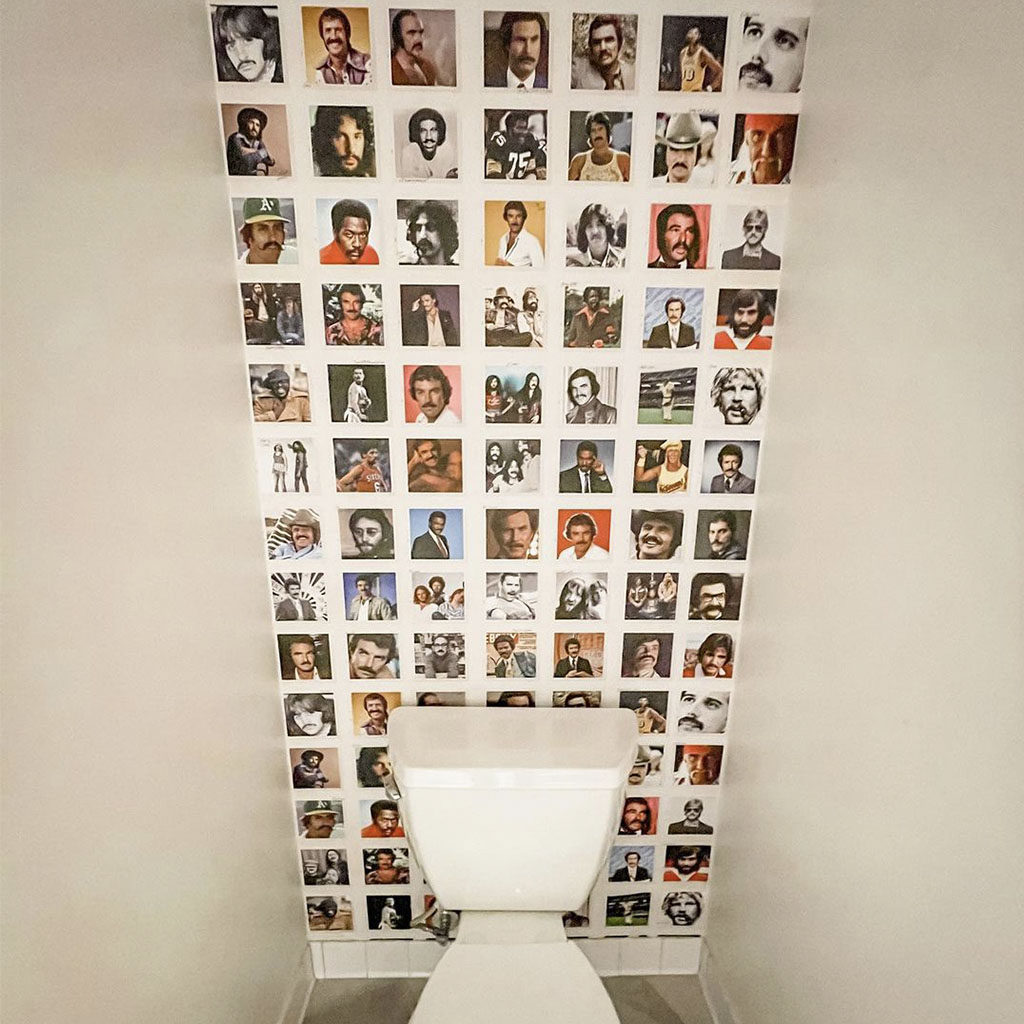 Toliet with wallpaper of various men with mustaches behind it