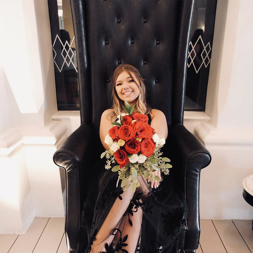 Woman holding red roses sitting in a oversized, black, tall back chair in the lobby of The Padre Hotel