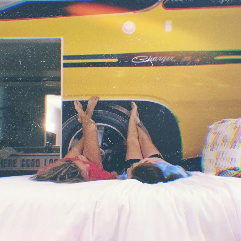 Two girls laying on a bed with their feet up on the Charger car artwork wall in a Rambler Motel guestroom