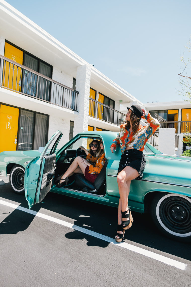 Woman leaning on the side of an old school sports car in Rambler Motel parking lot