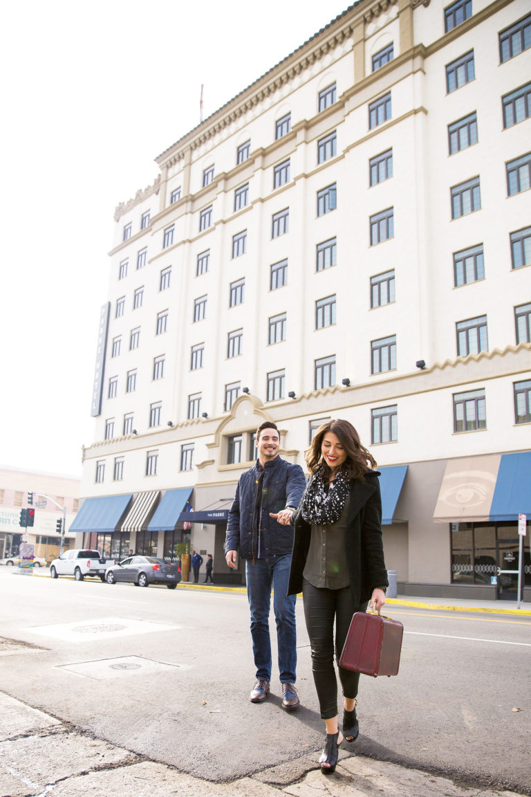 Woman with suitcase leading man across the street in front of the Padre Hotel