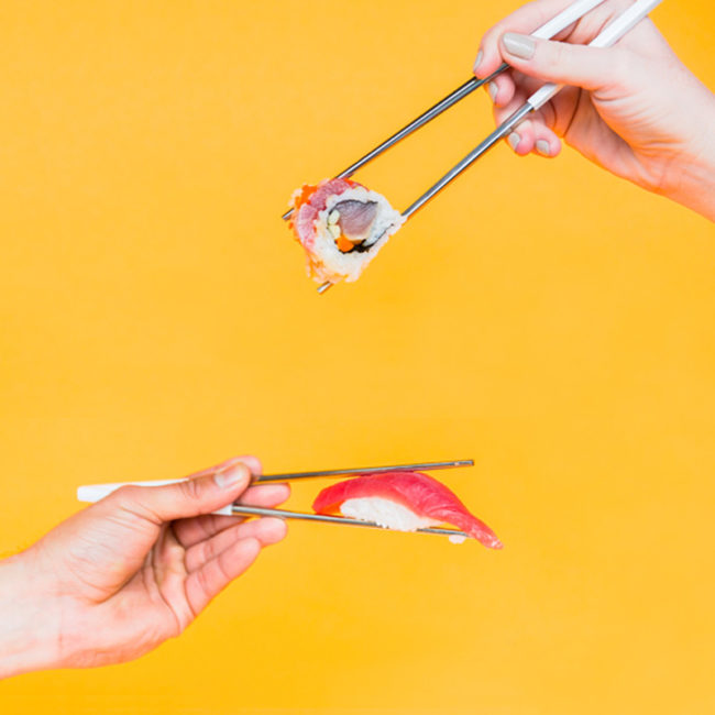 Two hands holding sushi with chopsticks against an orange background