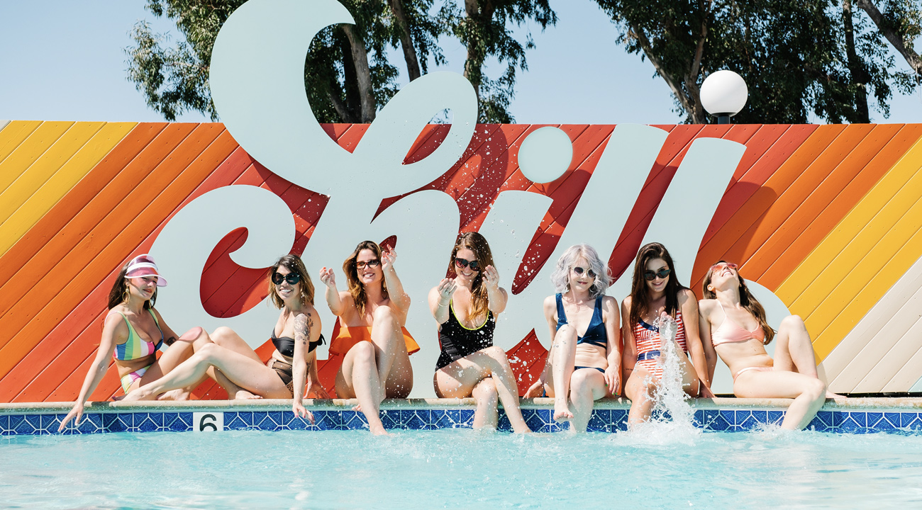 Group of girls in bathing suits sitting in front of the Rambler Motel's CHILL pool sign