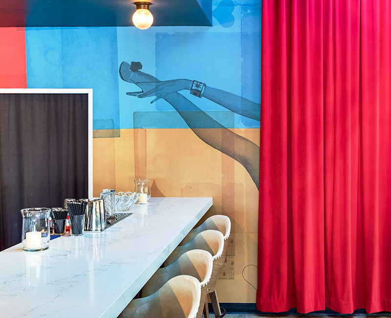 Bar table with cream chairs against a blue and gold background printed with a showgirl's leg peeking out of a red curtain