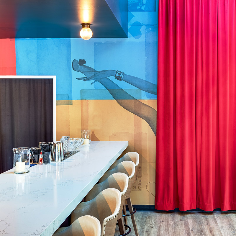 Bar table with cream chairs against a blue and gold background printed with a showgirl's leg peeking out of a red curtain