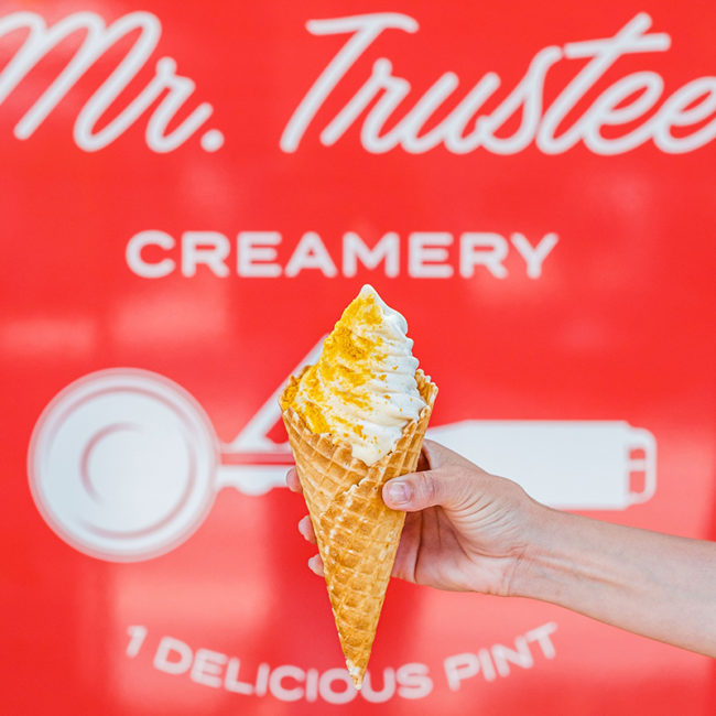 Hand holding waffle cone in front of Mr. Trustee branded sign
