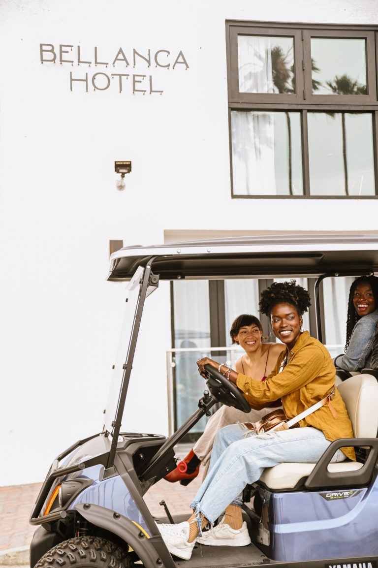 Group of women driving a golf cart in front of Bellanca Hotel